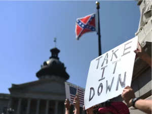 A confederate flag with a handmade sign that says take Ii down.